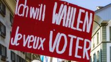 Rotes Plakat an einer Demonstration, auf dem in grossen weissen Buchstaben steht: "Ich will wählen" und darunter "Je veux voter"