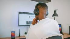 Mann ist von hinten zu sehen, wie er mit Kopfhörern vor einem PC-Bildschirm sitzt