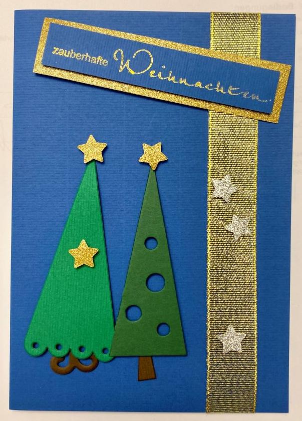 La carte de Noël bleue vue de près. On y voit deux sapins de Noël avec des étoiles et un ruban doré. Au-dessus, on peut lire: "zauberhafte Weihnachten" (en français: "Noël magique").