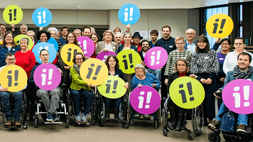 33 Personen mit verschiedenen Behinderungen halten Schilder mit Ausrufezeichen hoch.