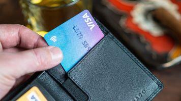 Nahaufnahme einer Hand, die eine Leder-Geldbörse öffnet und eine Visa-Kreditkarte herauszieht.