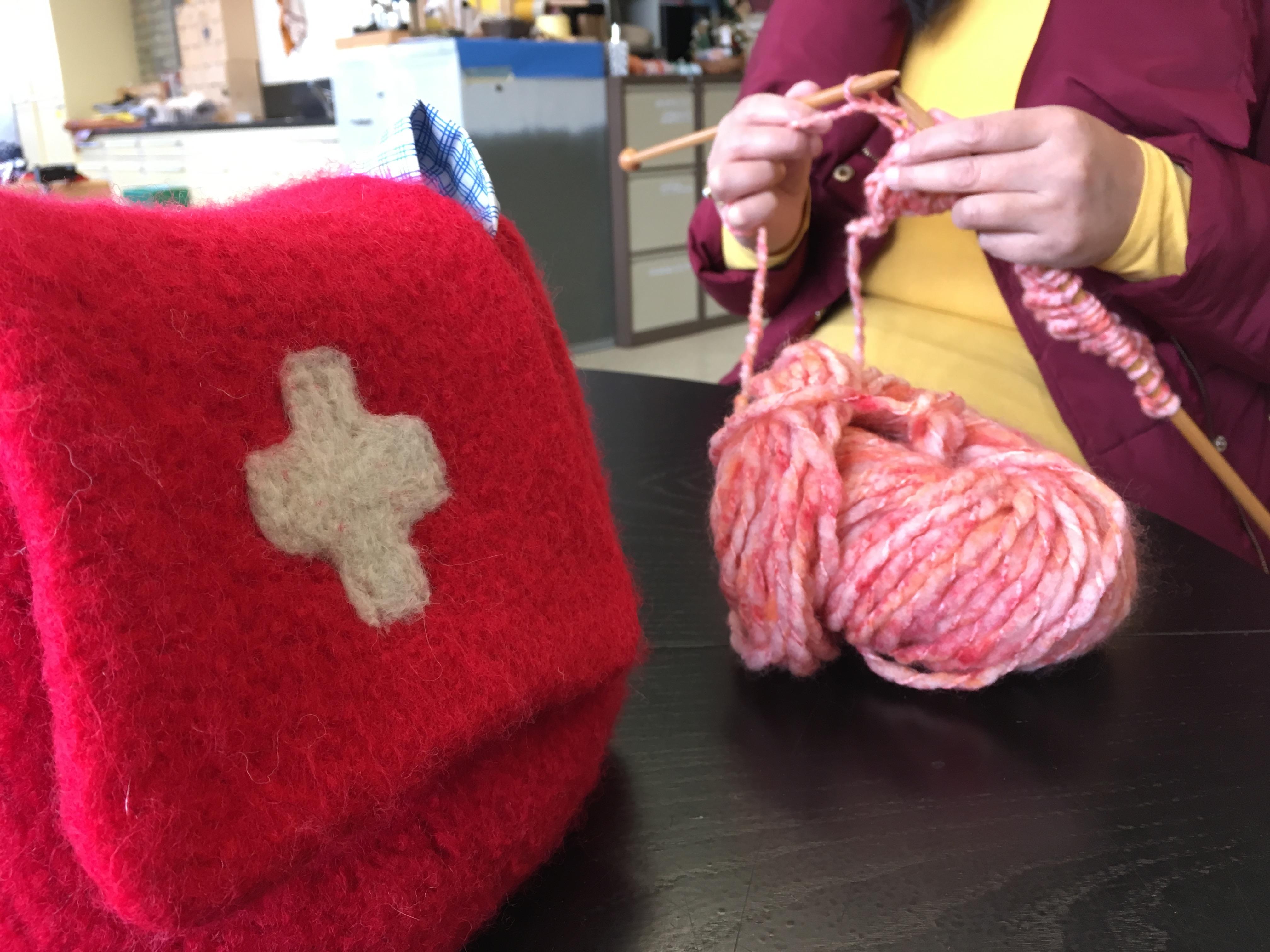 Eine rote Filztasche mit Schweizerkreuz, im Hindergrund die arbeitenden Händen einer BBZ-Benutzerin